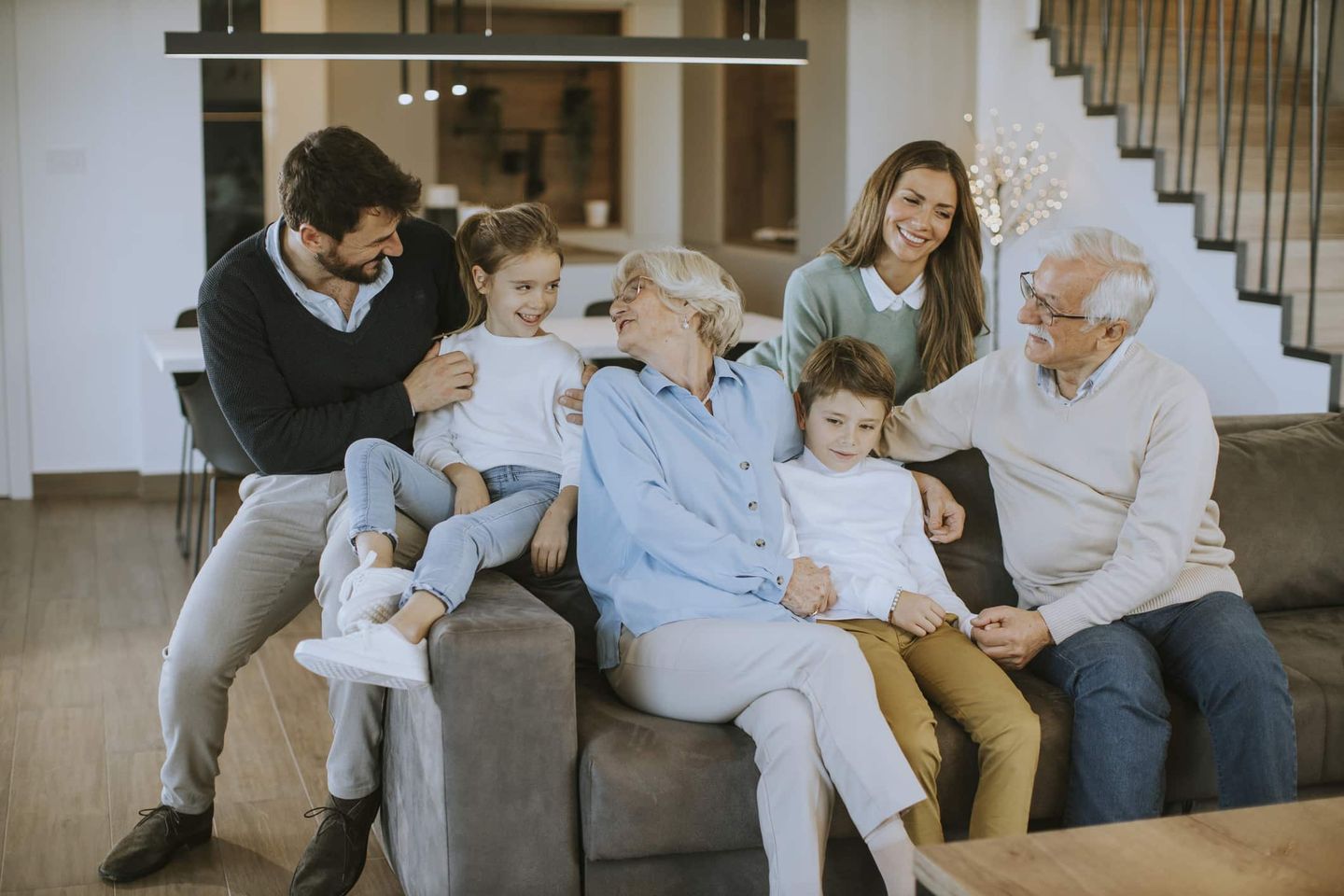 Mehrere Generationen einer Familie sitzen lachend zusammen auf einem Sofa im Wohnzimmer. Getty