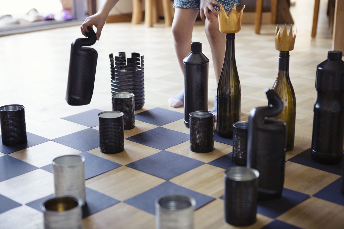 Ein handgemachtes Schachspiel mit Spielfiguren aus recycelten Flaschen, Dosen und Behältern auf einem Schachbrett aus schwarzem Papier.
