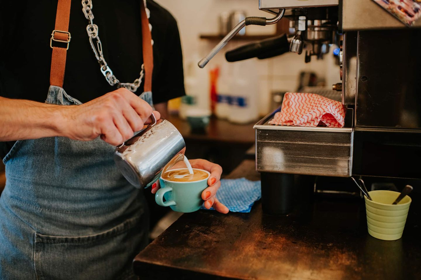Barista gießt Milch in eine Tasse Cappuccino an einer Espressomaschine. Getty