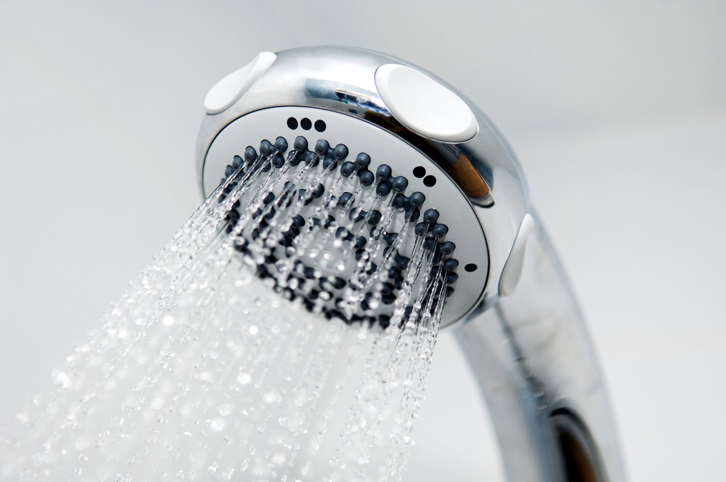 Nahaufnahme eines verchromten Duschkopfs mit mehreren feinen Wasserstrahlen vor hellem Hintergrund.