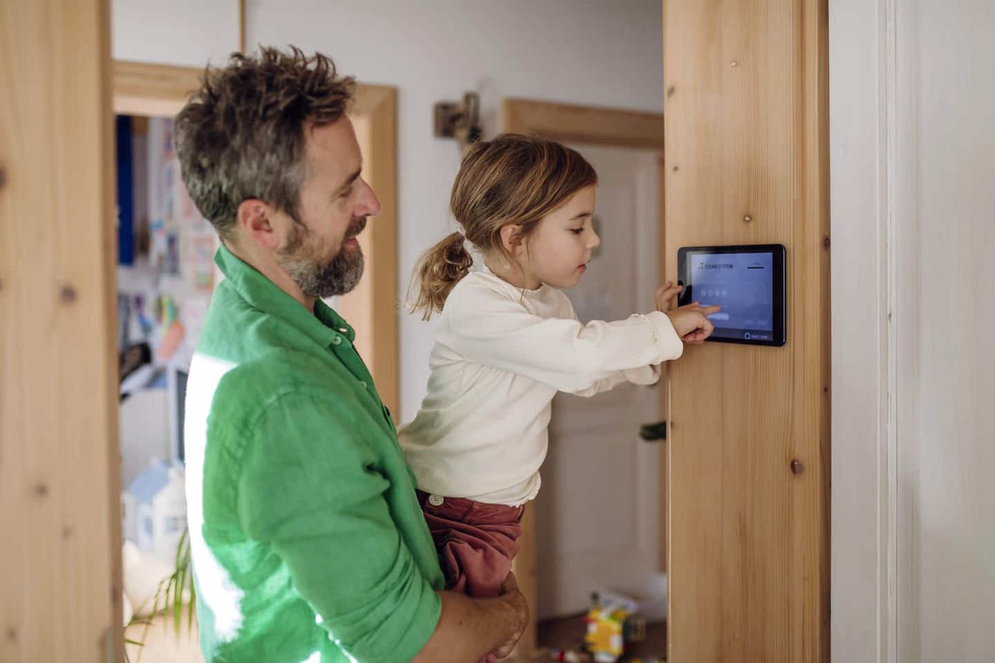 Vater und Tochter bedienen gemeinsam ein Smart-Home-Bedienpanel an der Wand. Getty