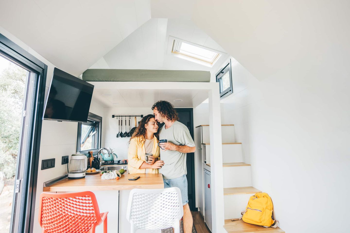 Junges Paar in gemütlicher Küche eines Tiny Houses, trinkt Kaffee und lacht