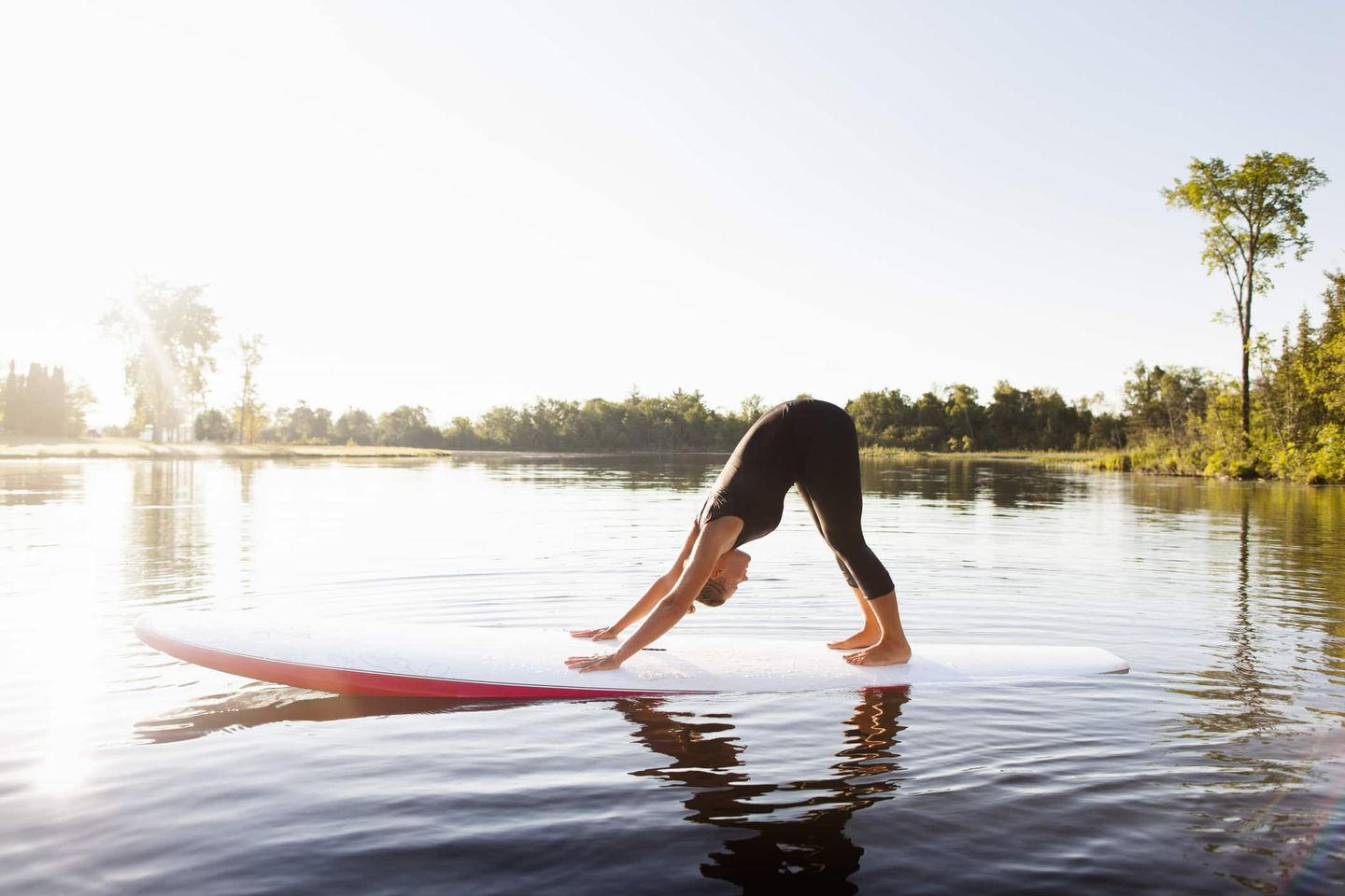 Frau praktiziert Yoga im herabschauenden Hund auf einem SUP-Board im sonnigen See Getty