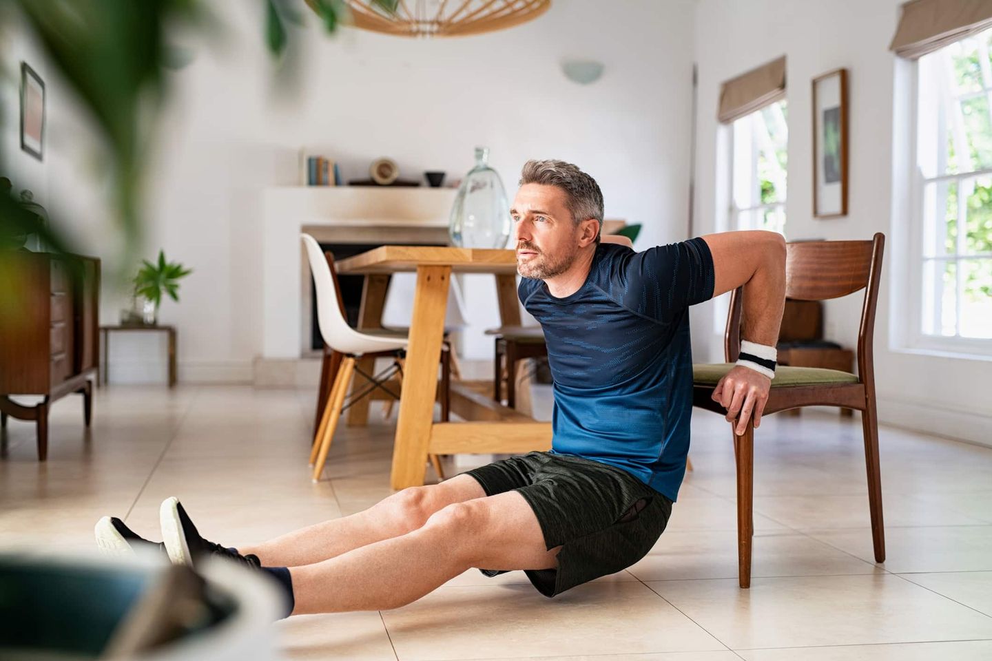 Mann macht Fitnessübung mit Stuhl im Wohnzimmer Getty