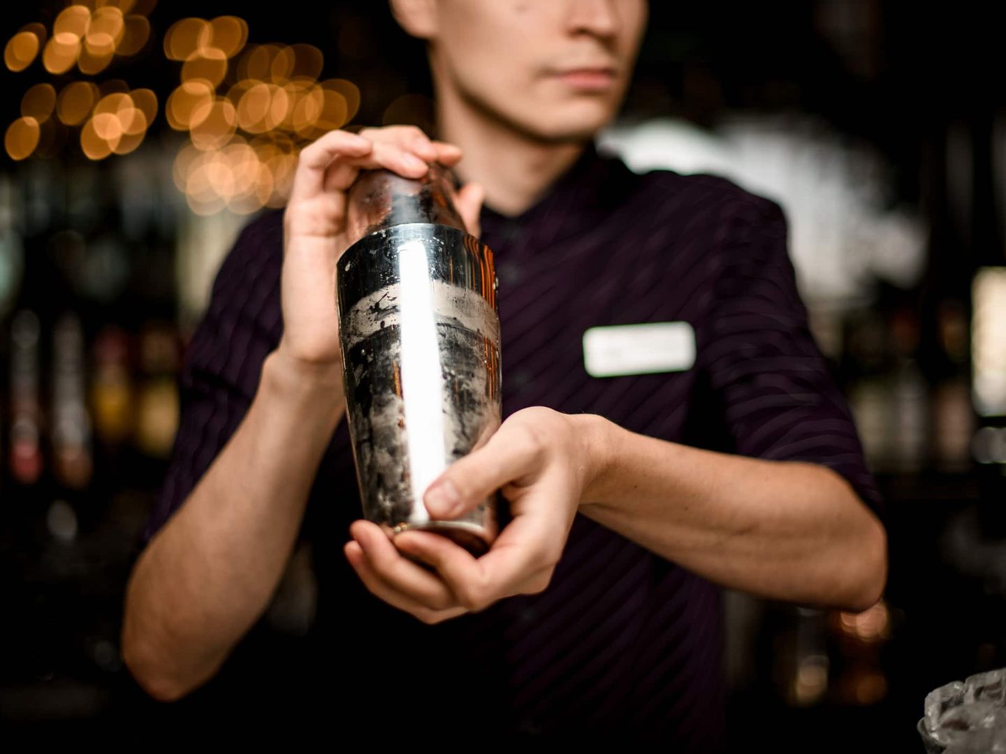 Ein Barkeeper schüttelt einen Cocktailshaker in einer Bar mit stimmungsvoller Beleuchtung. Getty