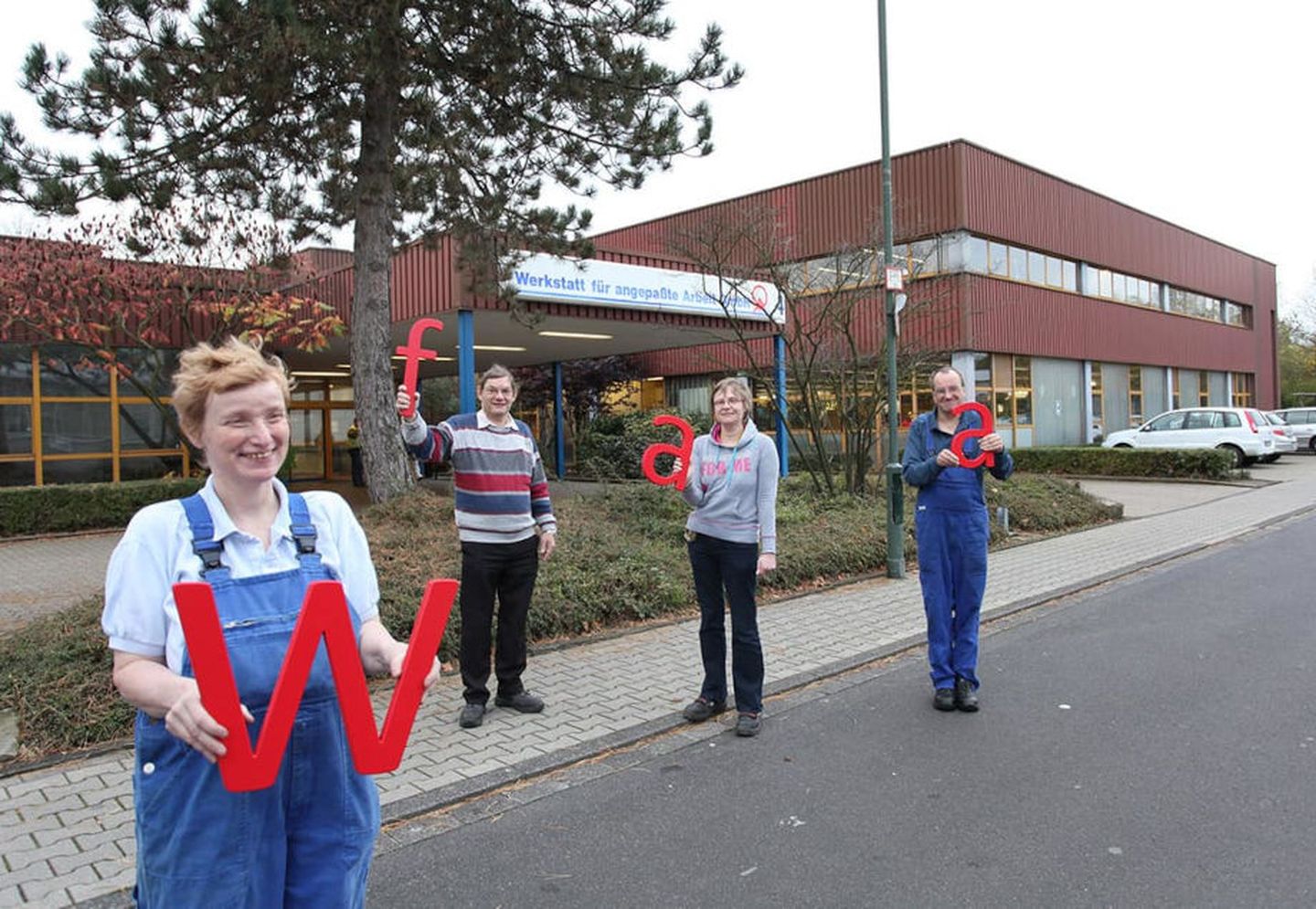 Werkstattbeschäftigte stehen vor dem Hauptsitz und halten die Buchstaben WfaA in der Hand © Werkstatt für angepasste Arbeit 