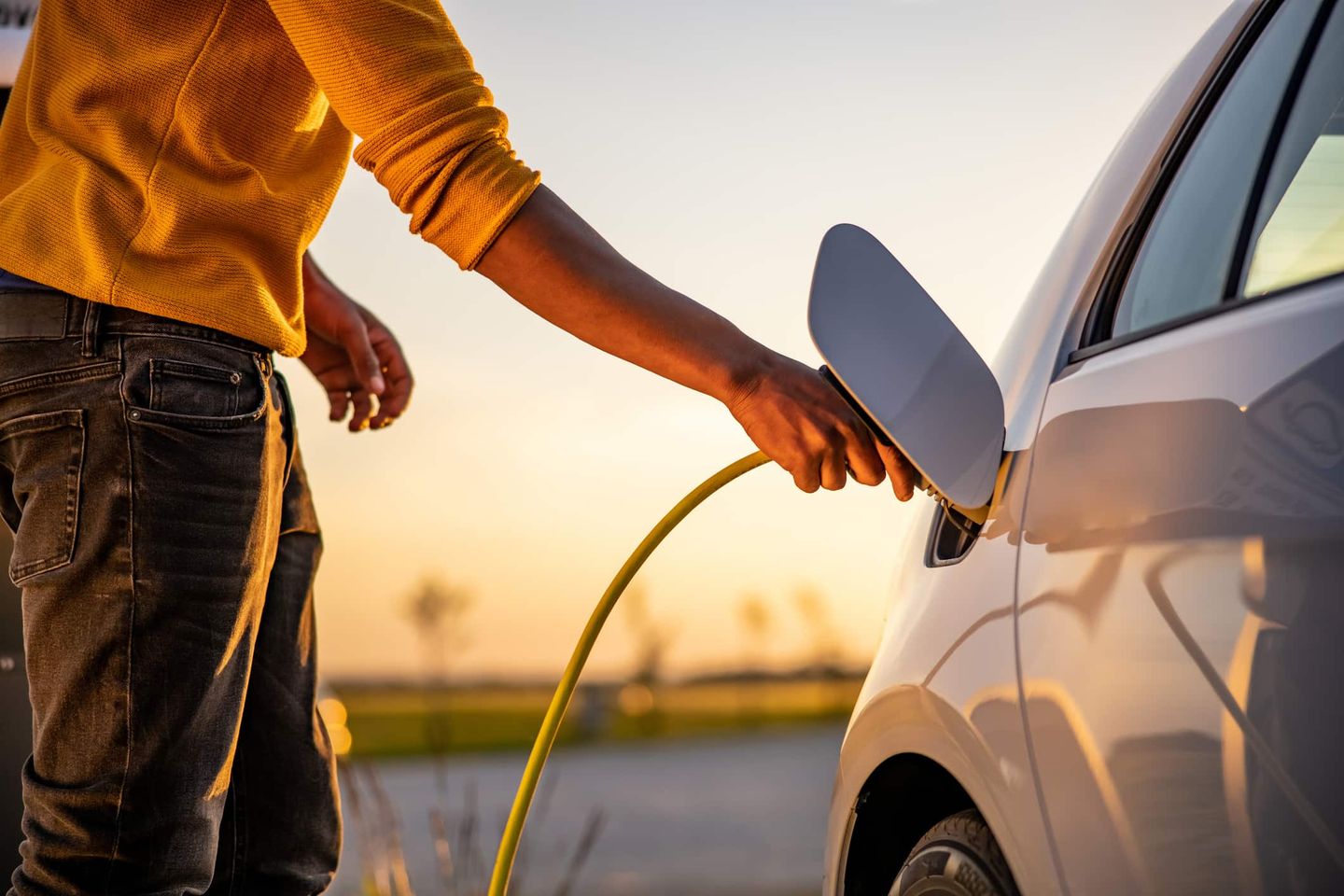 Person steckt ein Ladekabel in ein Elektroauto bei Sonnenuntergang. Getty