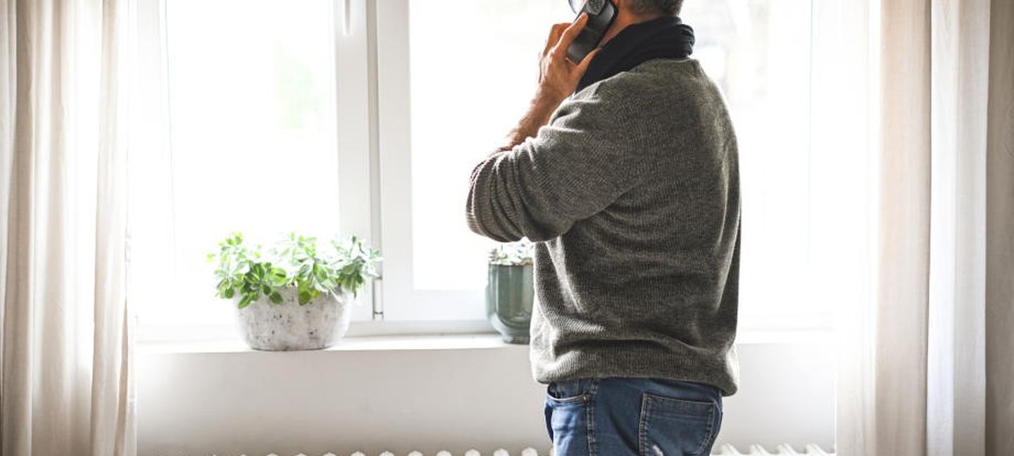 Gasarten: Ein Mann steht beim Telefonieren am Fenster und wärmt sich dabei an einer Heizung auf.