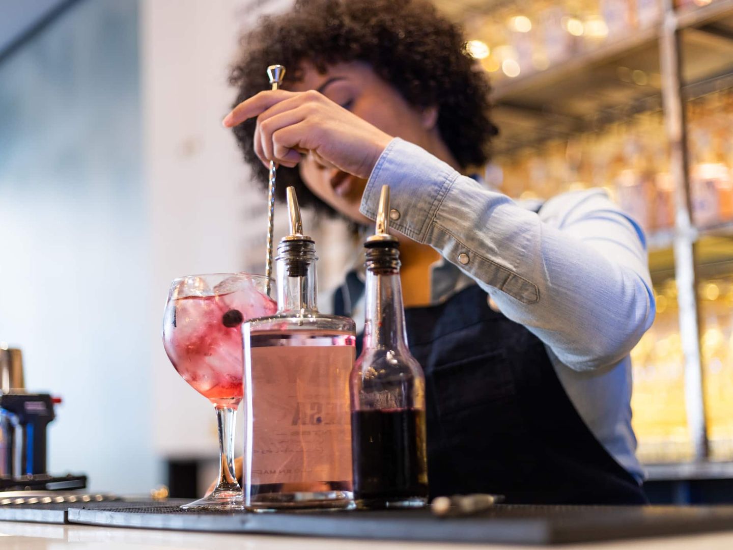 Eine Barkeeperin rührt einen Cocktail mit Eiswürfeln und Beeren in einem Glas um. Getty