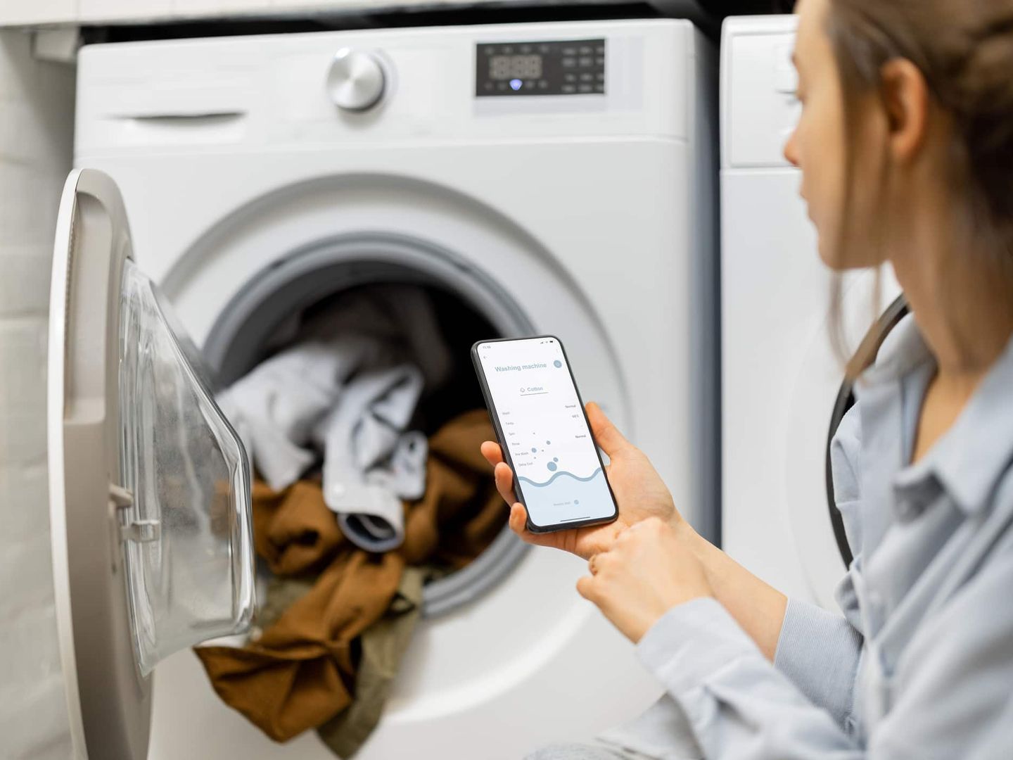 Frau überwacht eine Waschmaschine mit Hilfe einer Smart-Home-App auf ihrem Smartphone. Getty