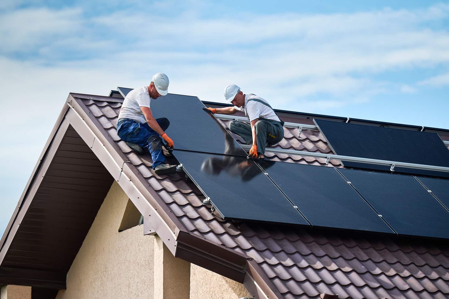 Zwei Handwerker montieren Solarpaneele auf einem Hausdach. Getty