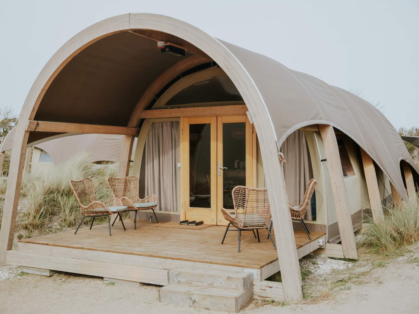 Modernes Glamping-Zelt mit Holzterrasse und Sitzmöbeln in den Dünen Getty