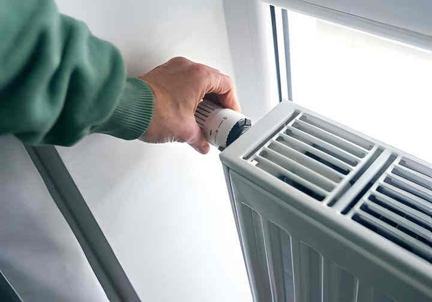 Eine Frau erhöht oder senkt die Temperatur am Heizkörper n der Wohnung. © Ekaterina Goncharova / Moment via via Getty Images