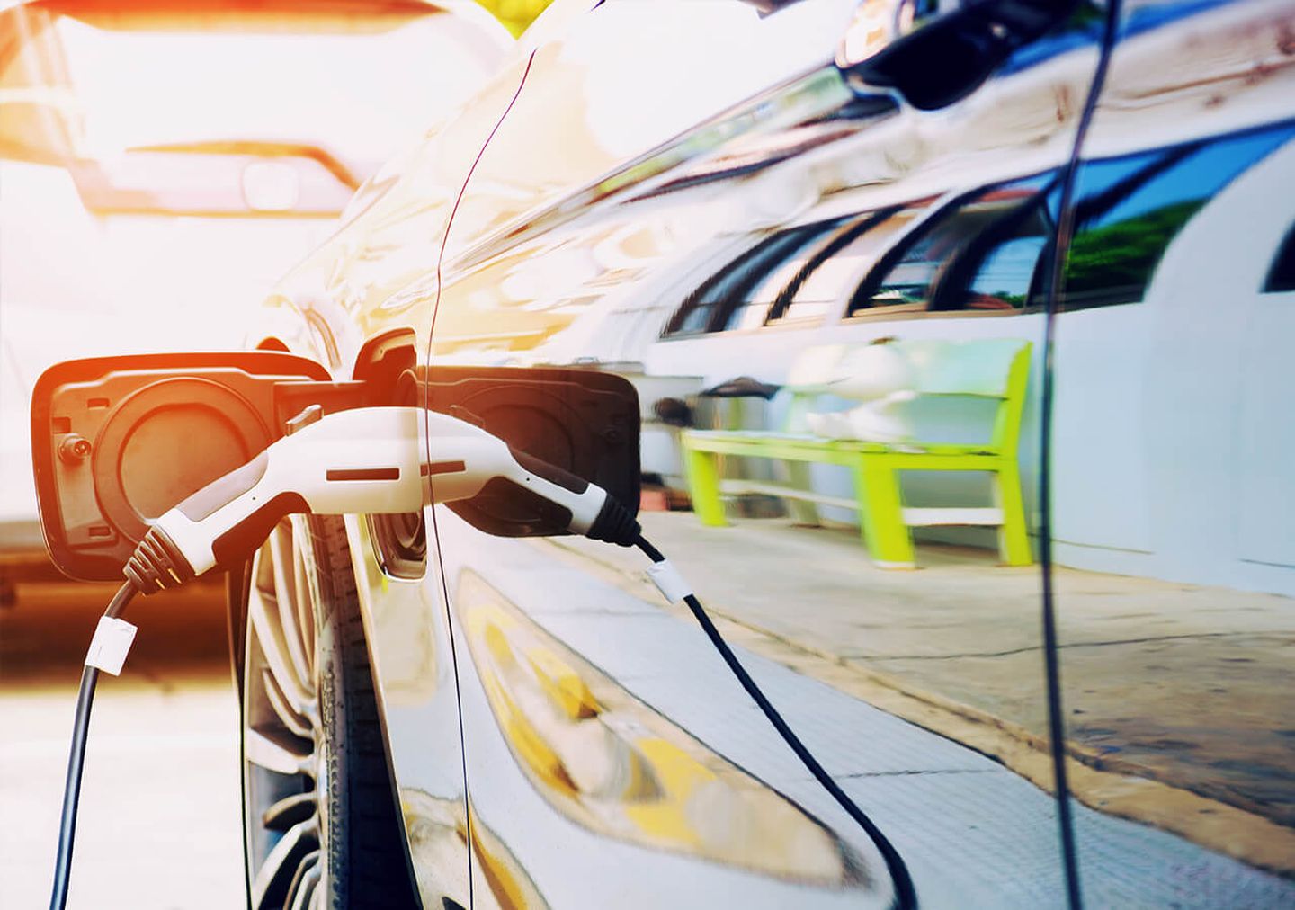 Ladestecker in E-Auto-Steckdose gesteckt. Im Lack der Autotür spiegelt sich eine giftgrüne Sitzbank.