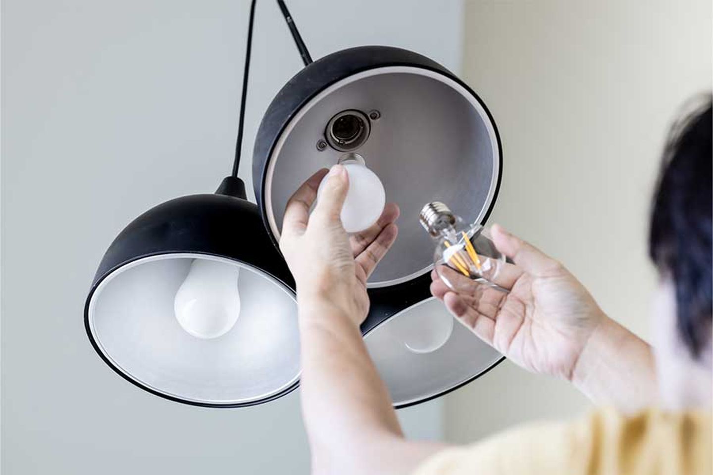 Eine Person tauscht bei einer Lampe die Glühbirnen aus. © panithan pholpanichrassamee/ Moment via Getty Images