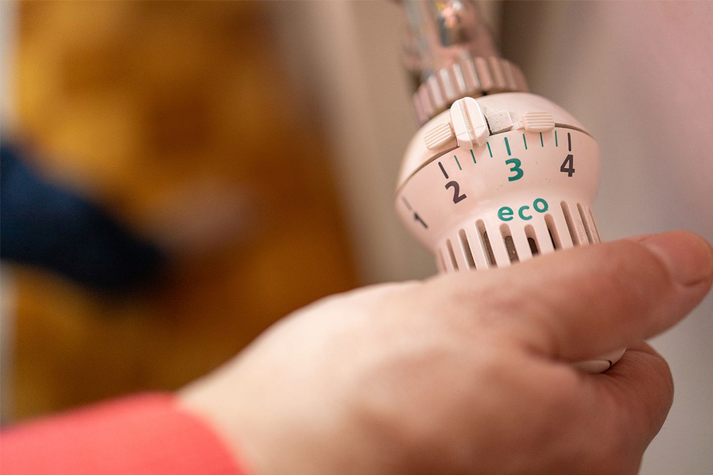 Nahaufnahme einer Hand, die das Thermostat eines elektrischen Heizkörpers auf Eco-Modus dreht, um Heizkosten zu sparen. © Kate Wieser / Moment via Getty Images