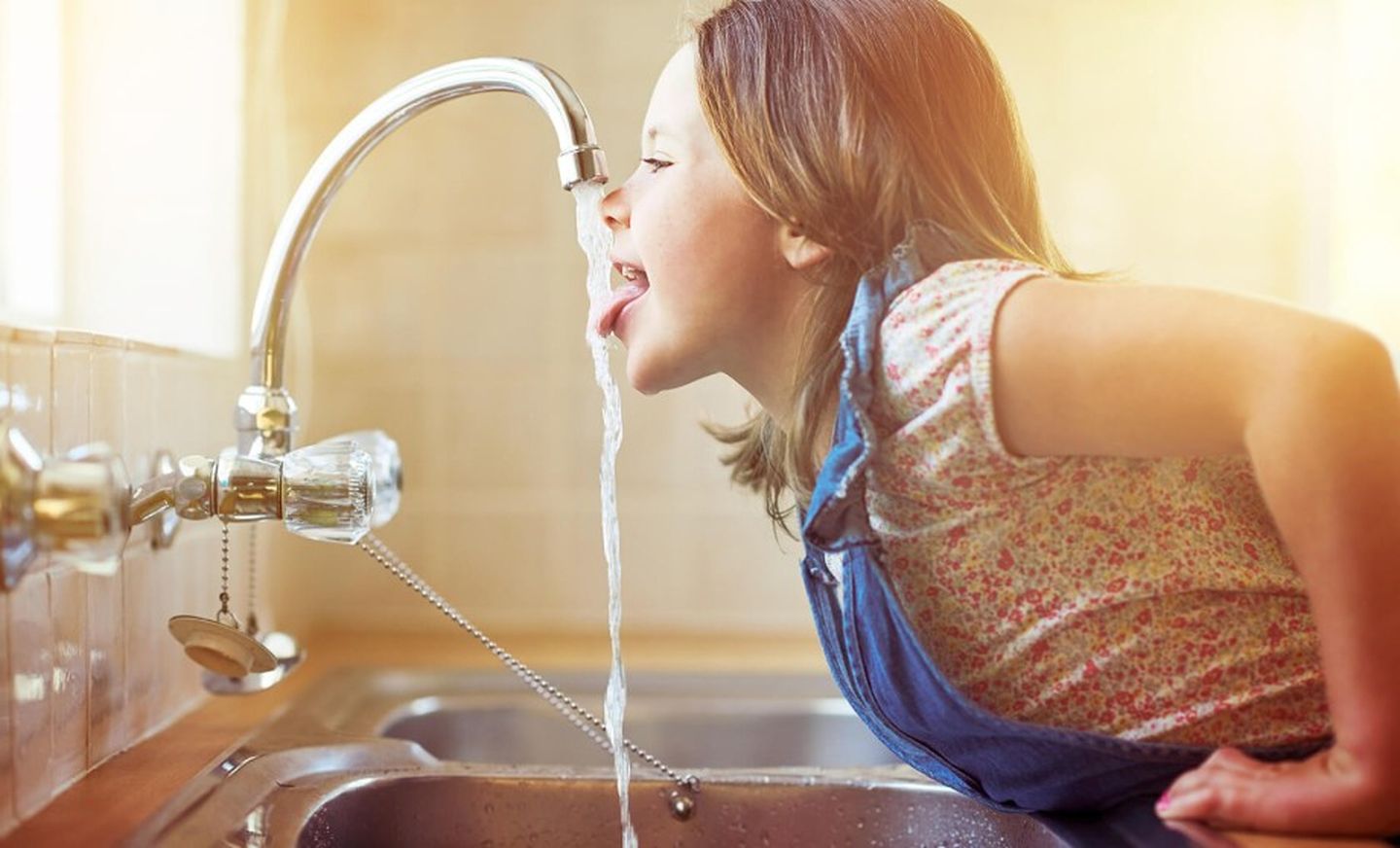 Ein Mädchen trinkt Wasser vom Wasserhahn