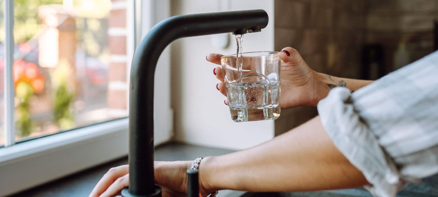 Eine füllt eine Flasche am Wasserhahn