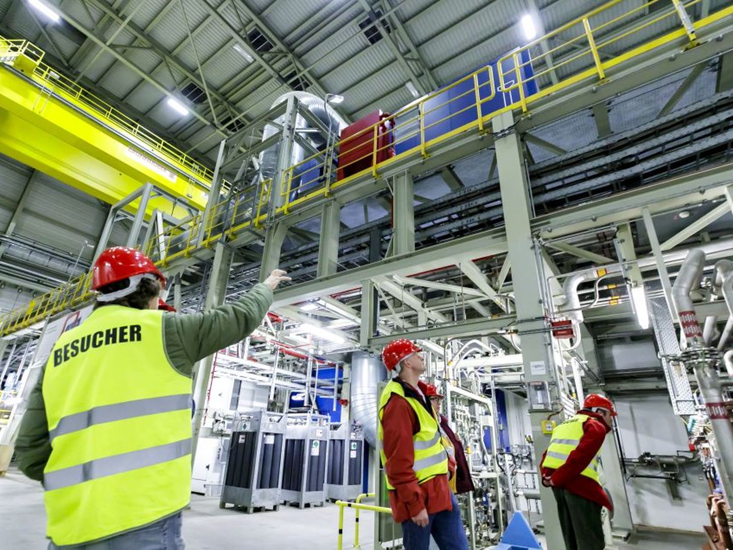 Besuchergruppe mit Schutzhelmen und Westen in einer großen Industriehalle mit Rohrleitungen und Krananlage. © Stadtwerke Düsseldorf © Stadtwerke Düsseldorf