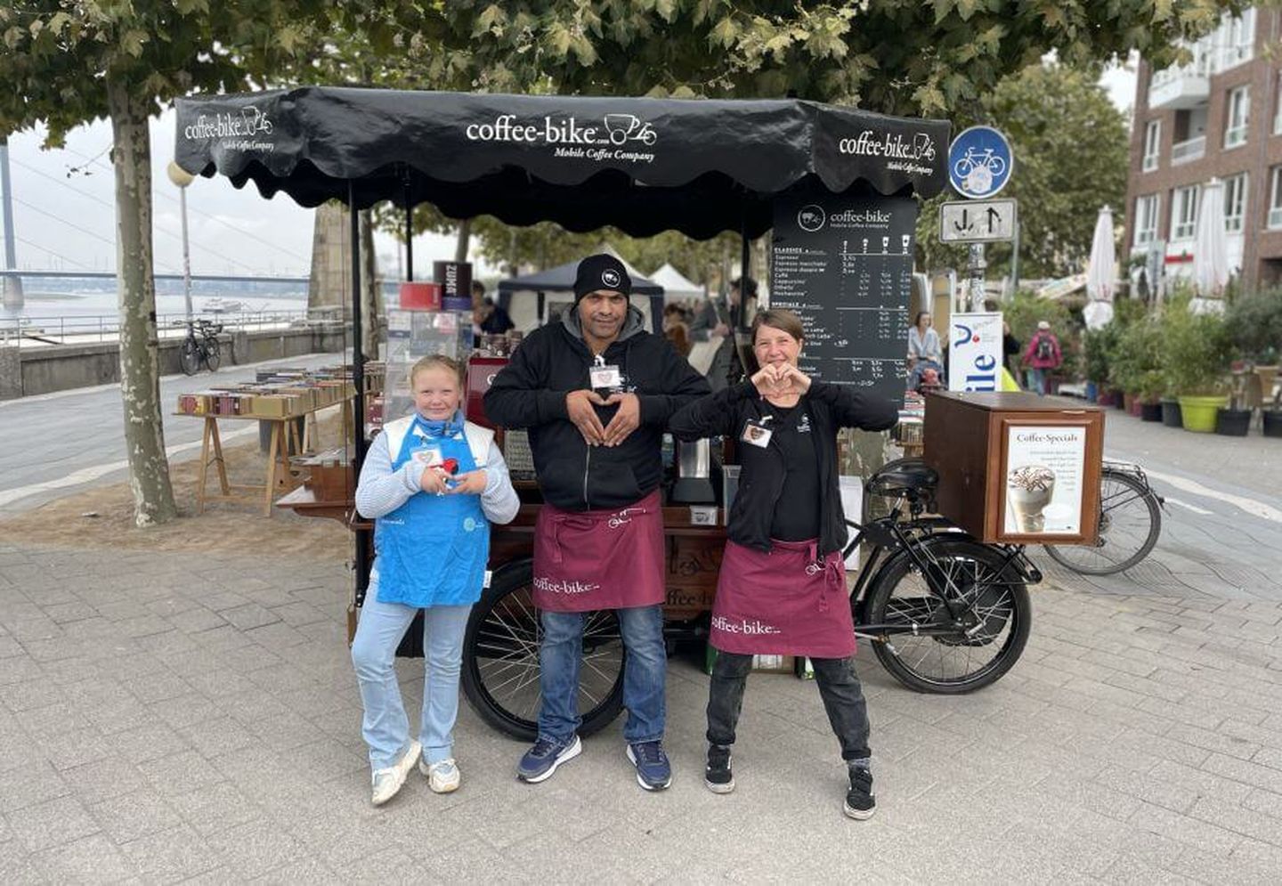 Drei Menschen posieren vor einem „coffee bike“ an der Rheinuferpromenade in Düsseldorf. Claudia Adams / Altstadt Marketing GmbH